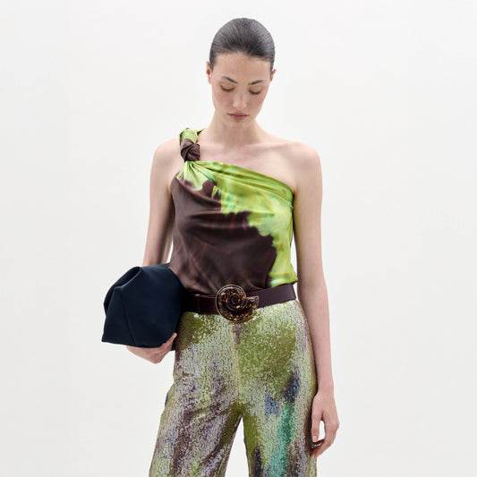 A woman wearing the Yanet Blouse, a green and brown silk top with an asymmetric neckline, paired with matching pants.