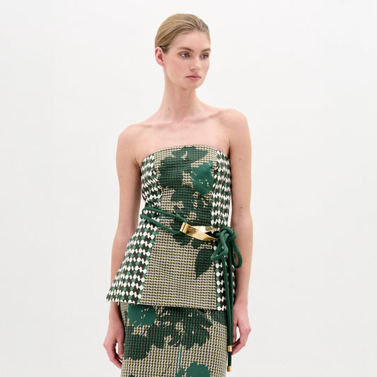 A woman wears the Astor Top, a strapless bustier in green, beige, and houndstooth Italian fabric with a matching skirt and a green belt with gold clasp, standing against a plain white background.