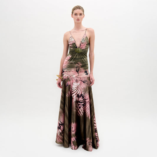 A woman poses against a plain background wearing the Carmin Dress— a floor-length, sleeveless maxi crafted from Italian fabric with a pink and olive green tie-dye pattern and a deep V neckline.