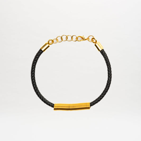 The Hadria Necklace is shown on a plain white background, featuring a black braided leather design with a gold clasp and gold embellishments.