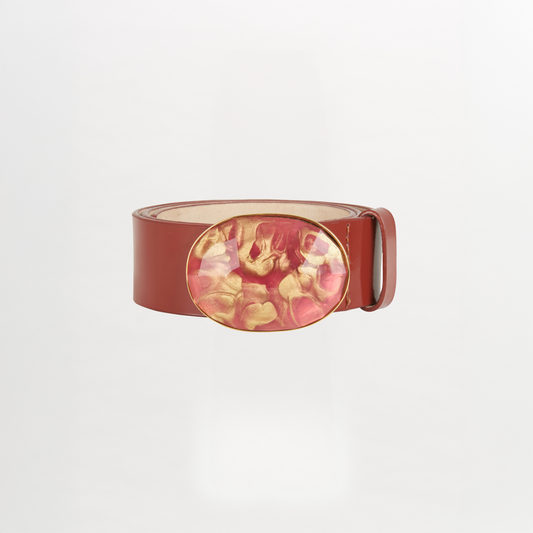 The Irene Belt Camel features glossy brown Italian leather, a wide strap, and a large oval resin buckle with a pink and gold marbled design. Shown on a white background, it's the standout accessory for Fall 2023.