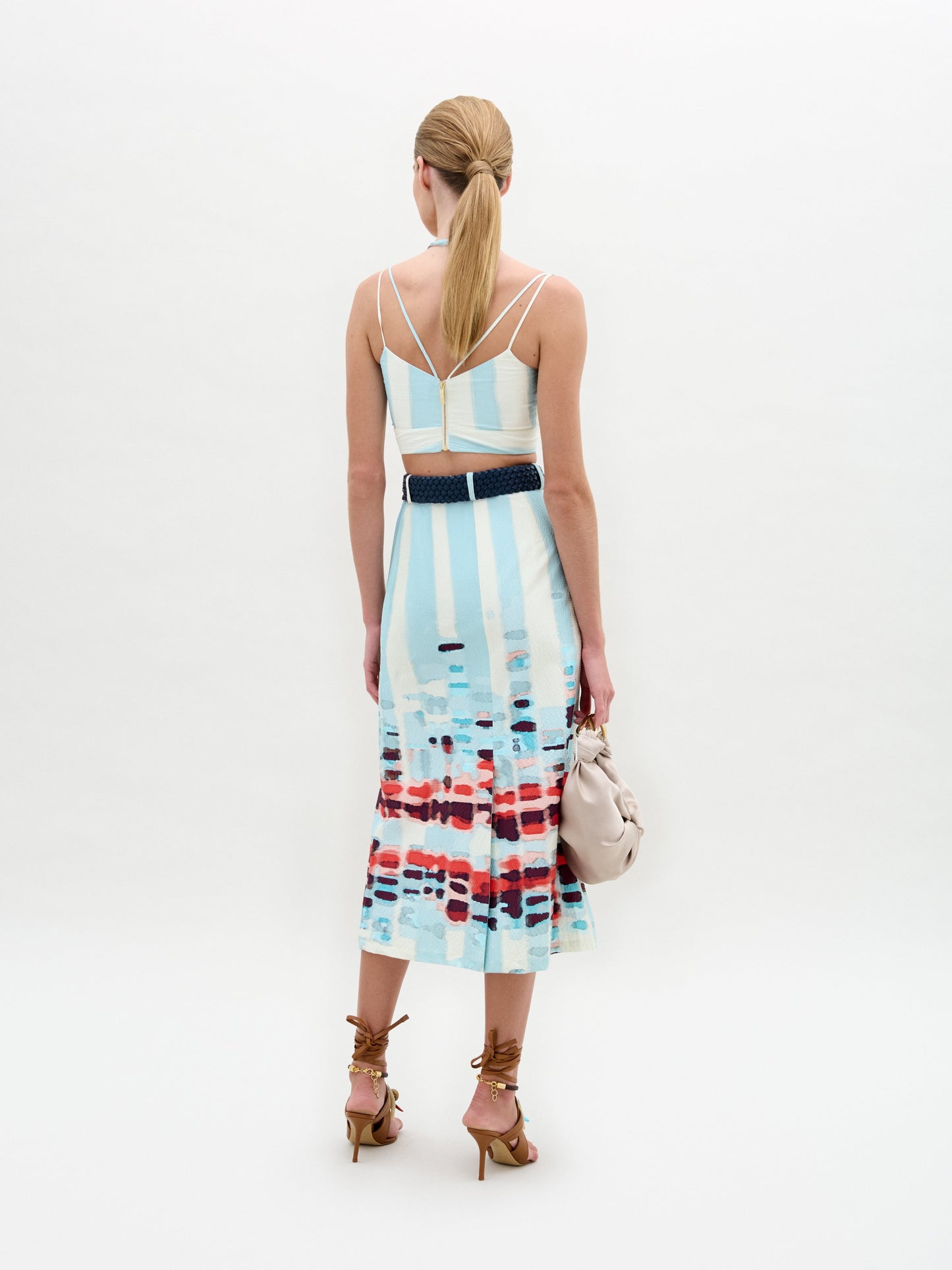 A person wears the Layan Skirt as a sleeveless patterned dress, paired with a beige bag and tassel-adorned strappy sandals.