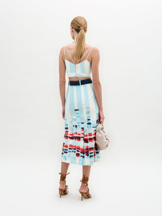 A person wears the Layan Skirt as a sleeveless patterned dress, paired with a beige bag and tassel-adorned strappy sandals.