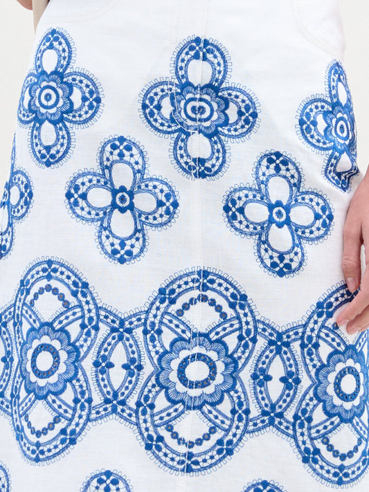A person wearing a white top with the Layan Skirt, holding a beige jacket.