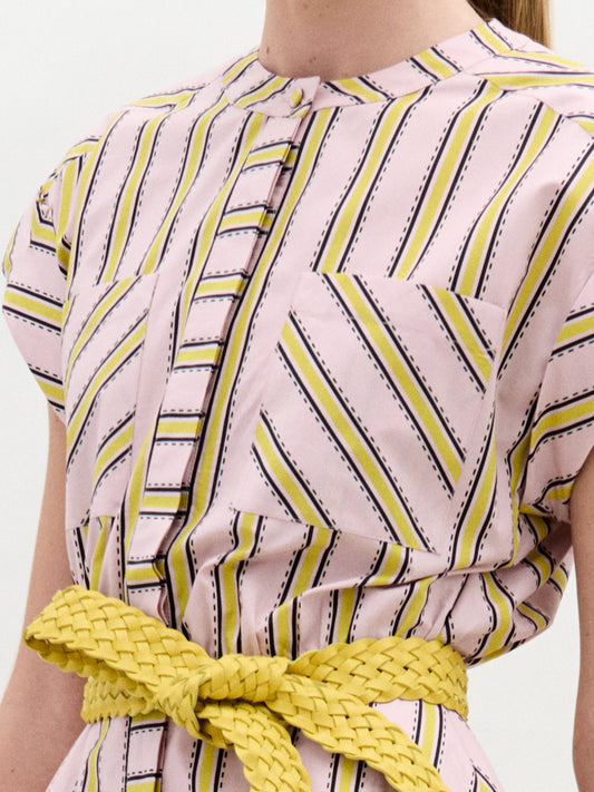 A woman models the Macarena Dress—a light pink and yellow geometric midi made from Italian fabric—styled with a woven leather belt and high-heeled sandals, set against a plain white background.