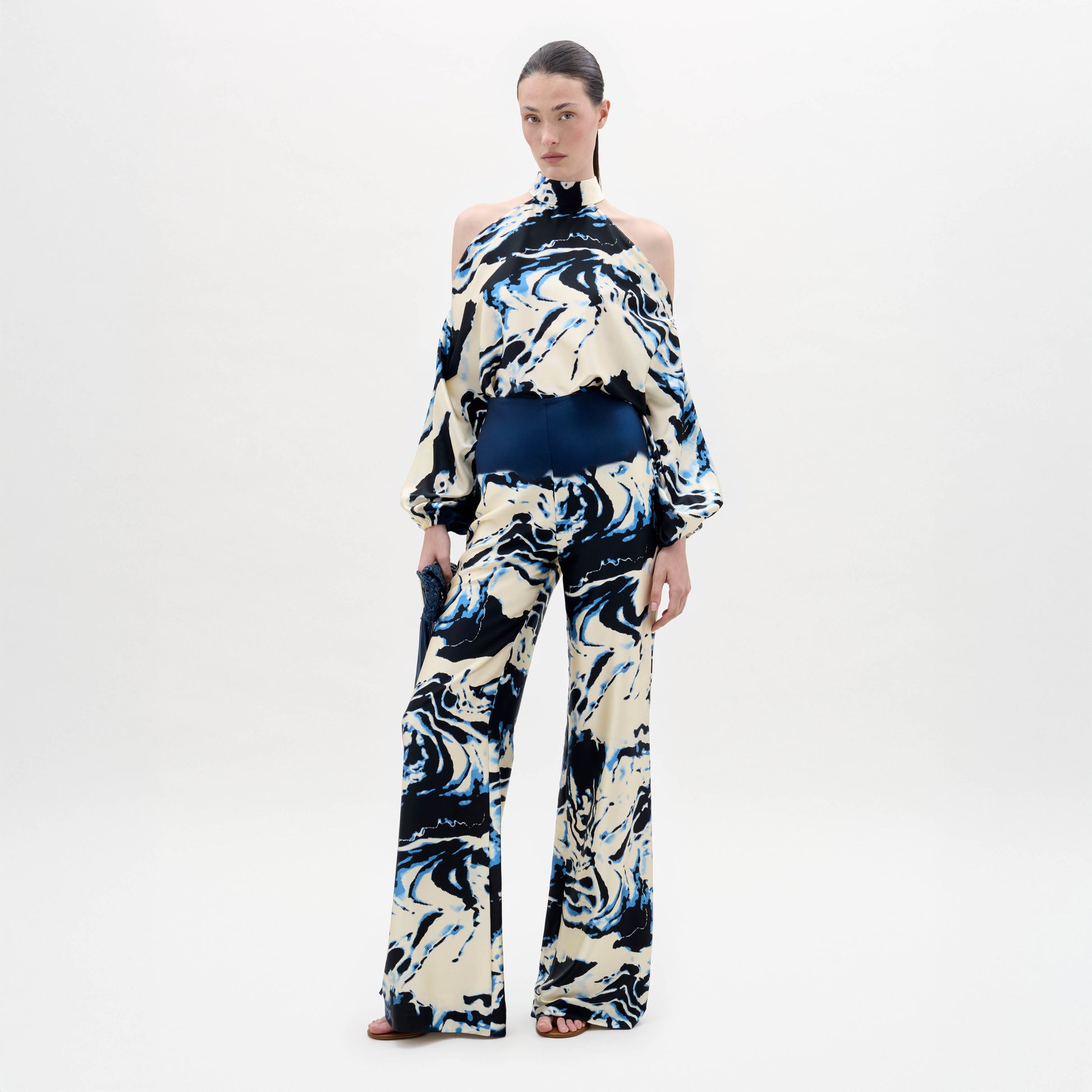 A woman stands against a plain white background wearing a cream and navy blue marble-patterned halter top with matching Como Pants in a wide-leg style.