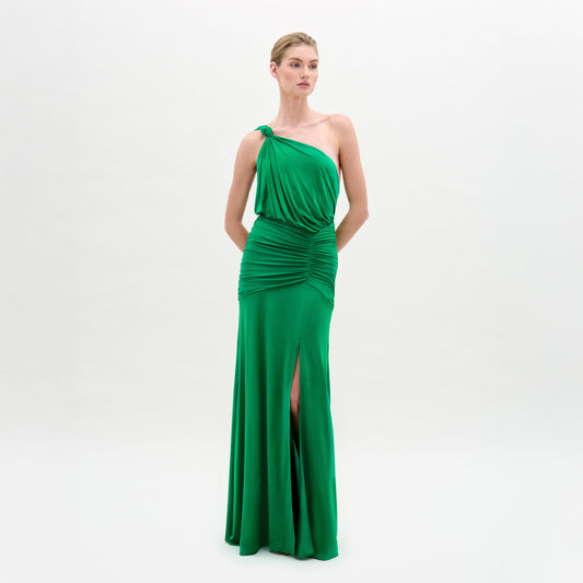 A woman stands against a plain white background wearing the Antara Dress—a bright green, fitted maxi with an asymmetric one-shoulder neckline, gathered waist, and front slit.