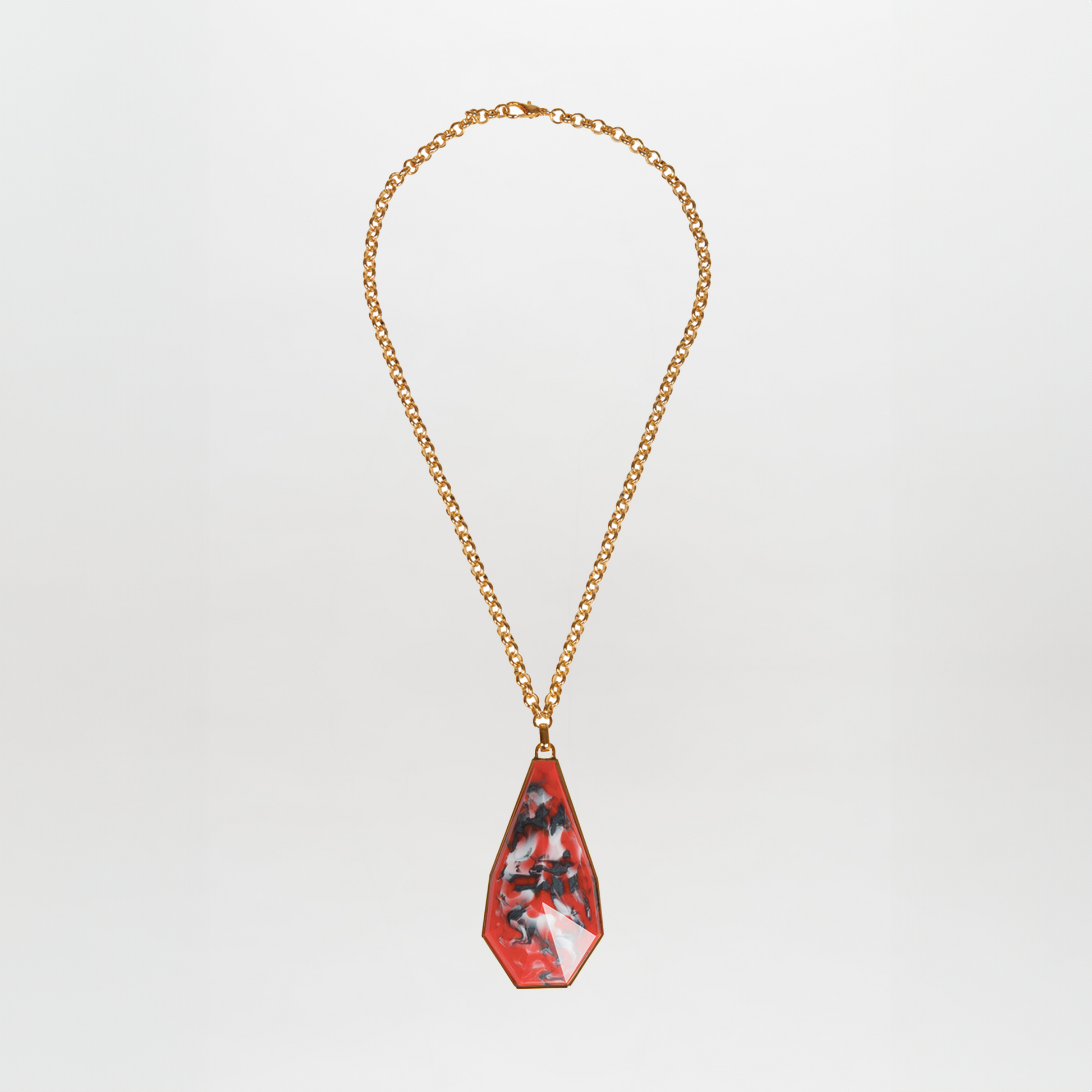 The Ascoli Necklace is a gold chain accessory with a triangular pendant showcasing a marbled red, black, and white pattern made from Petralux® fantasy stone.