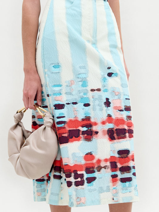 A person wears the Layan Skirt as a sleeveless patterned dress, paired with a beige bag and tassel-adorned strappy sandals.