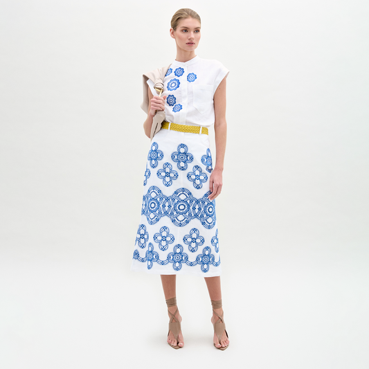 A person wearing a white top with the Layan Skirt, holding a beige jacket.