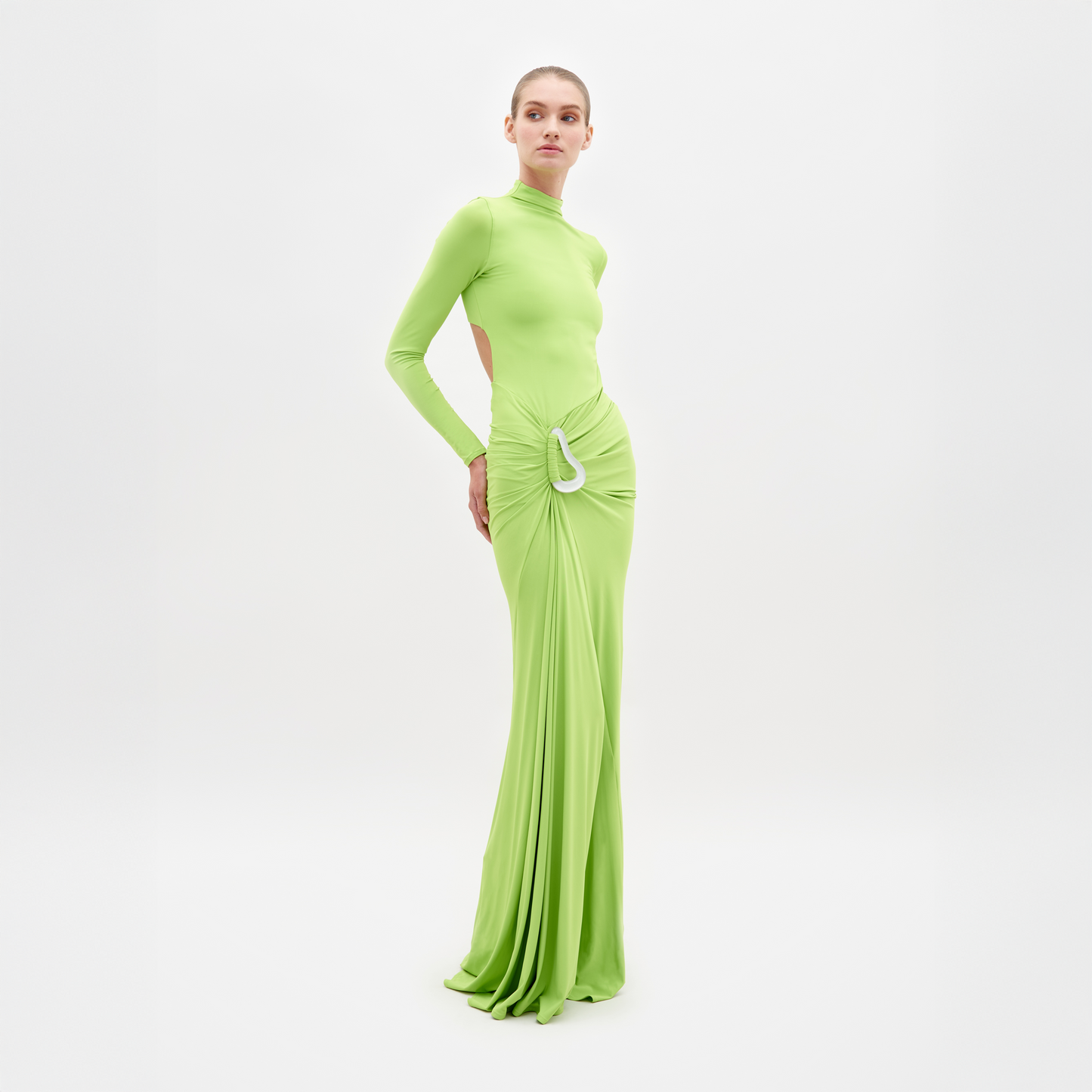 A person is wearing the Lena Dress Lime, a long, lime green dress with long sleeves and a high neckline. The dress, which is available for shipping by February 15th, features cut-out details at the sides and a gathered, draped front. White background.